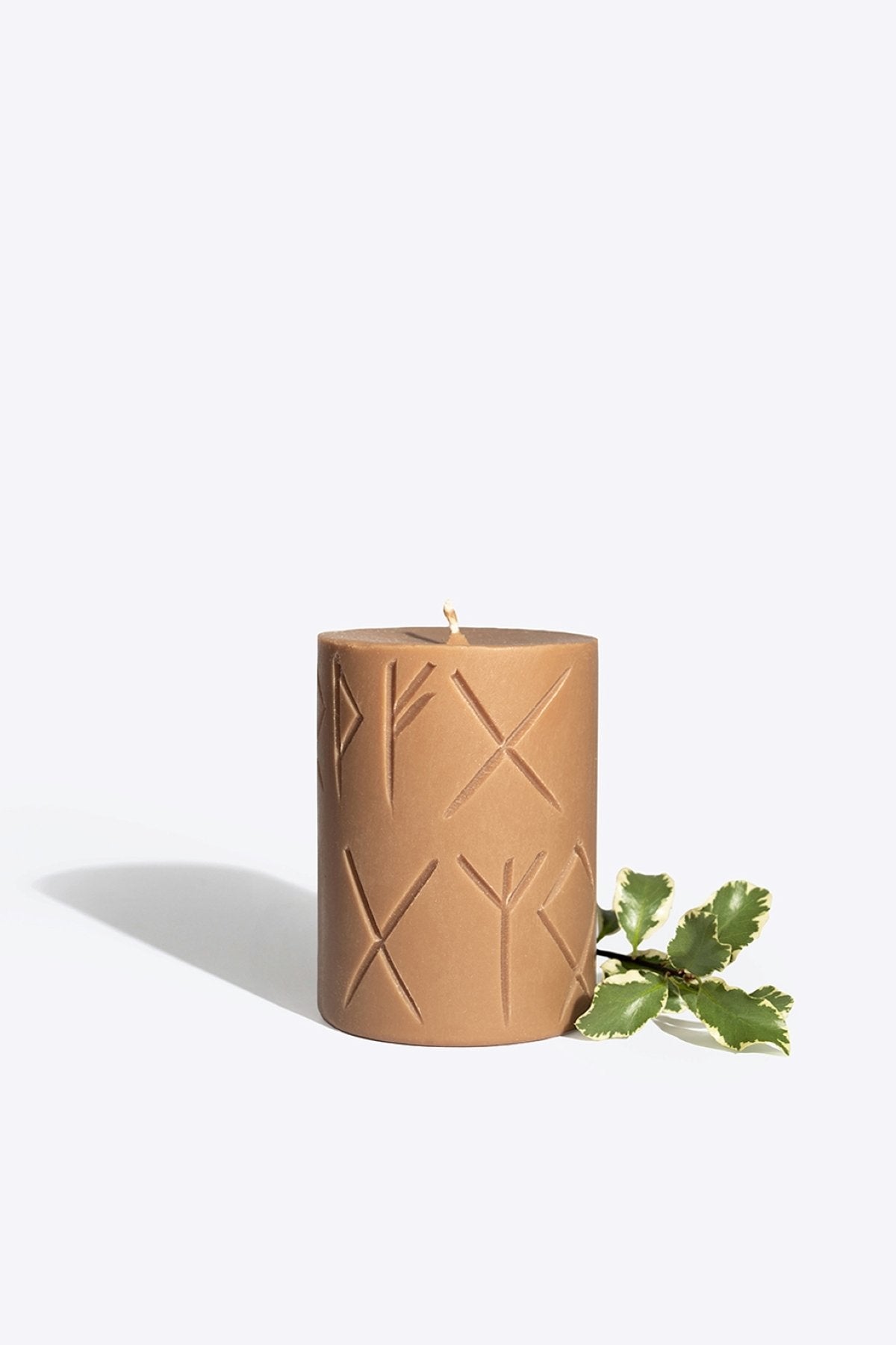 1. Handcrafted Rune candle FRIGGA in brown soy wax with rune carvings, shown with green leaves