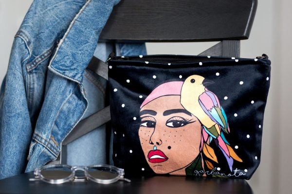 2. Garbanota black makeup bag with artistic print, styled with gloves, watch, and wallet on wooden floor