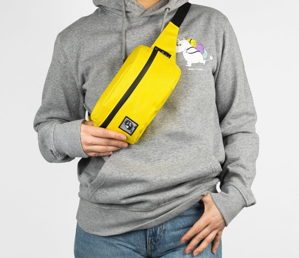 1. Person wearing yellow waist bag with black zipper across chest, dressed in grey hoodie with Moomin print