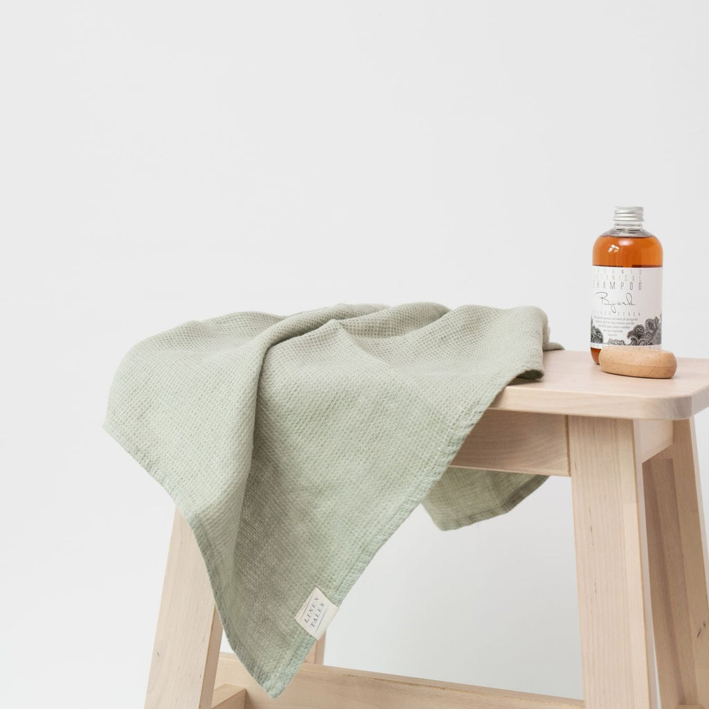 6. Sage green waffle linen towel on a stool with a bottle of bath oil and soap