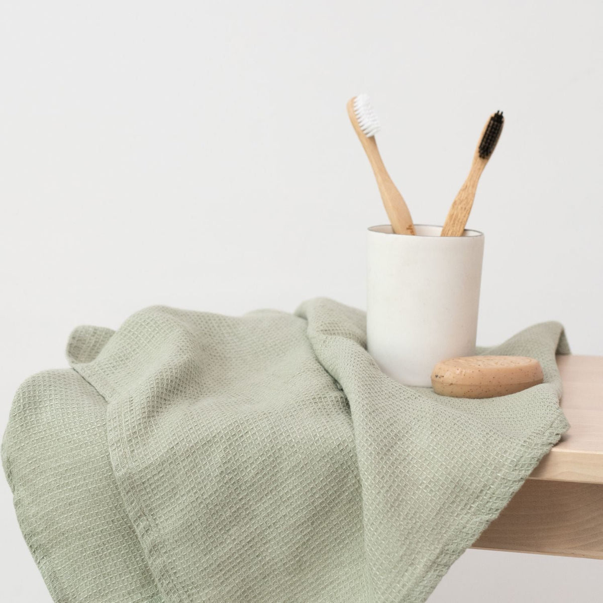 5. Sage green waffle linen towel draped over a stool with toothbrushes in a cup