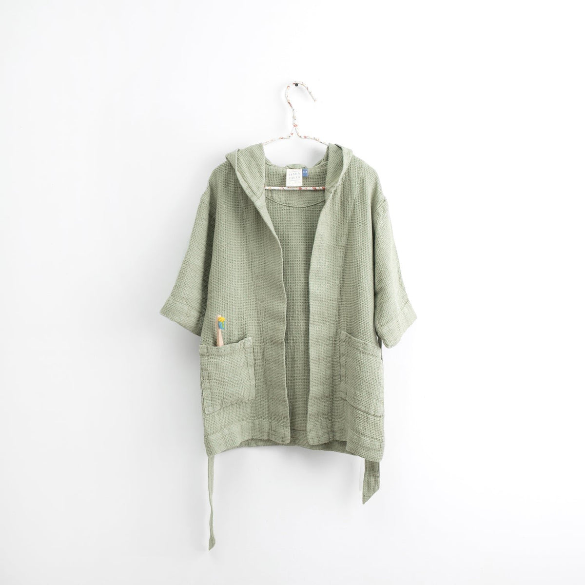 2. Kids sage green linen bathrobe with hood and pockets hanging on white background