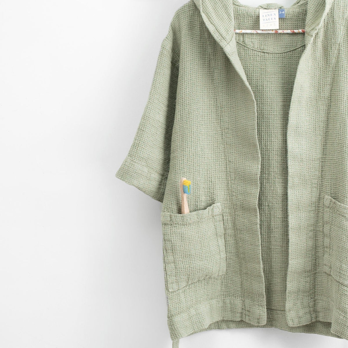 3. Close-up of sage green linen bathrobe showing pocket with toothbrush