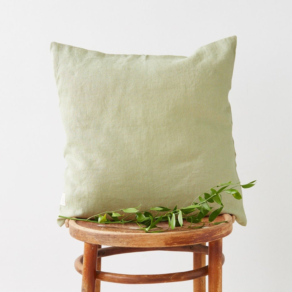 6. Sage green Linen Tales cushion cover on a wooden chair with green foliage