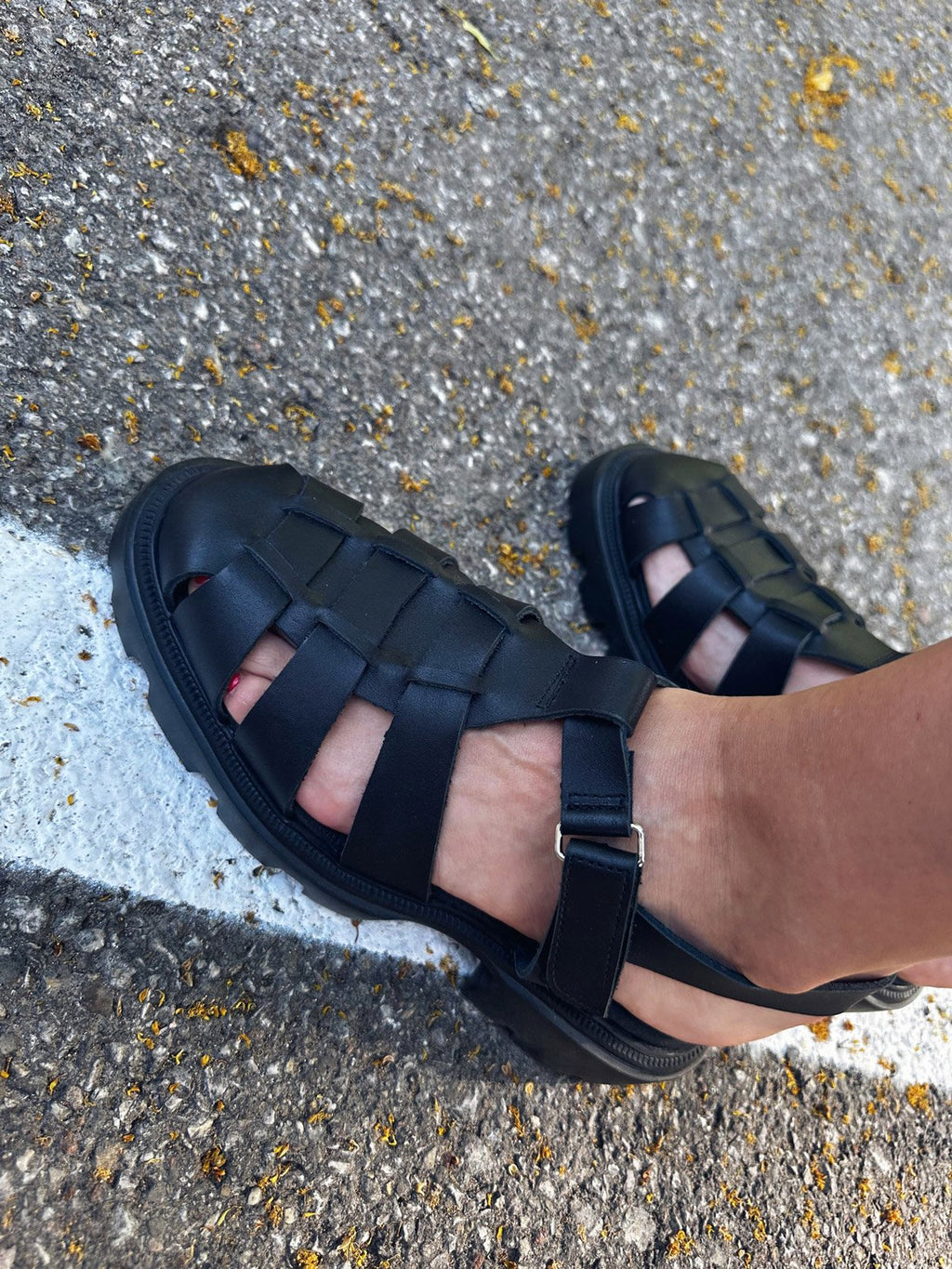 7. Close-up of women's black woven leather Samelin sandals on pavement