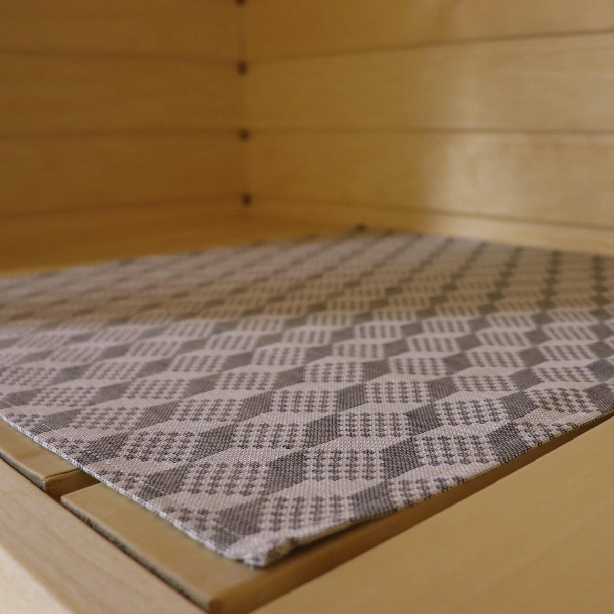 1. Close-up of LOKO sauna bench seating pad with traditional Viru County mitten pattern in grey, placed on wooden sauna bench