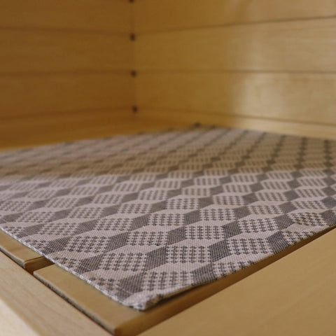 1. Close-up of LOKO sauna bench seating pad with traditional Viru County mitten pattern in grey, placed on wooden sauna bench