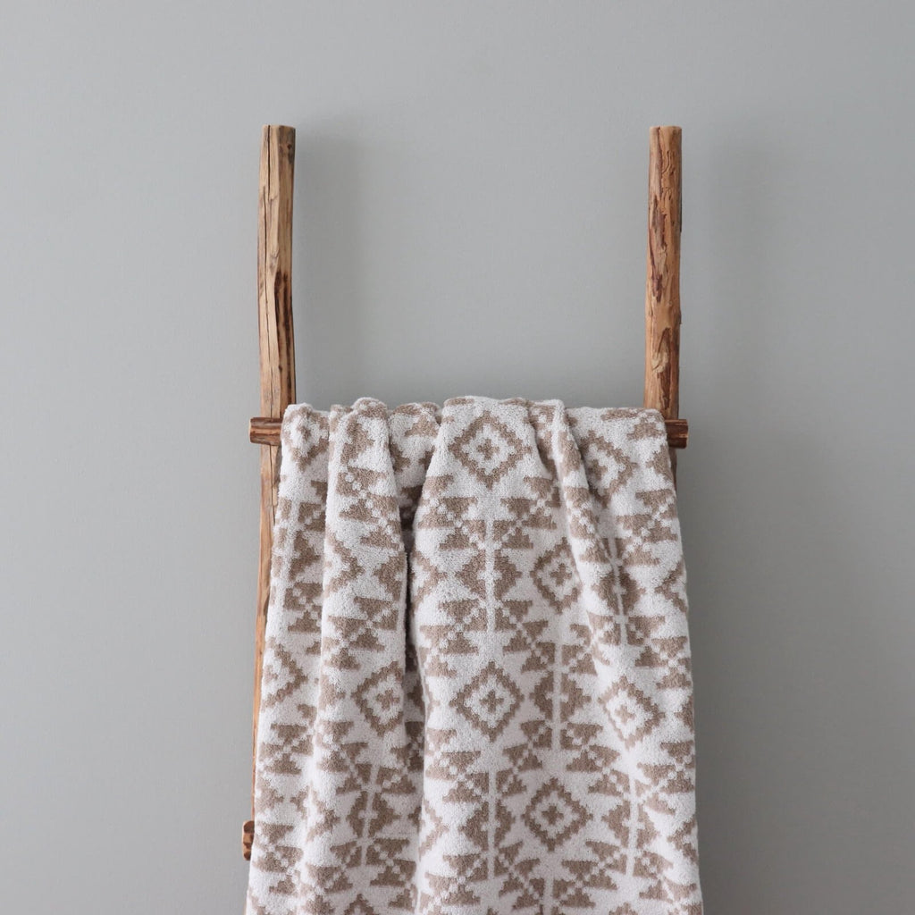 2. Beige and white terry sauna towel with Harju County mitten pattern hanging on wooden ladder against grey wall