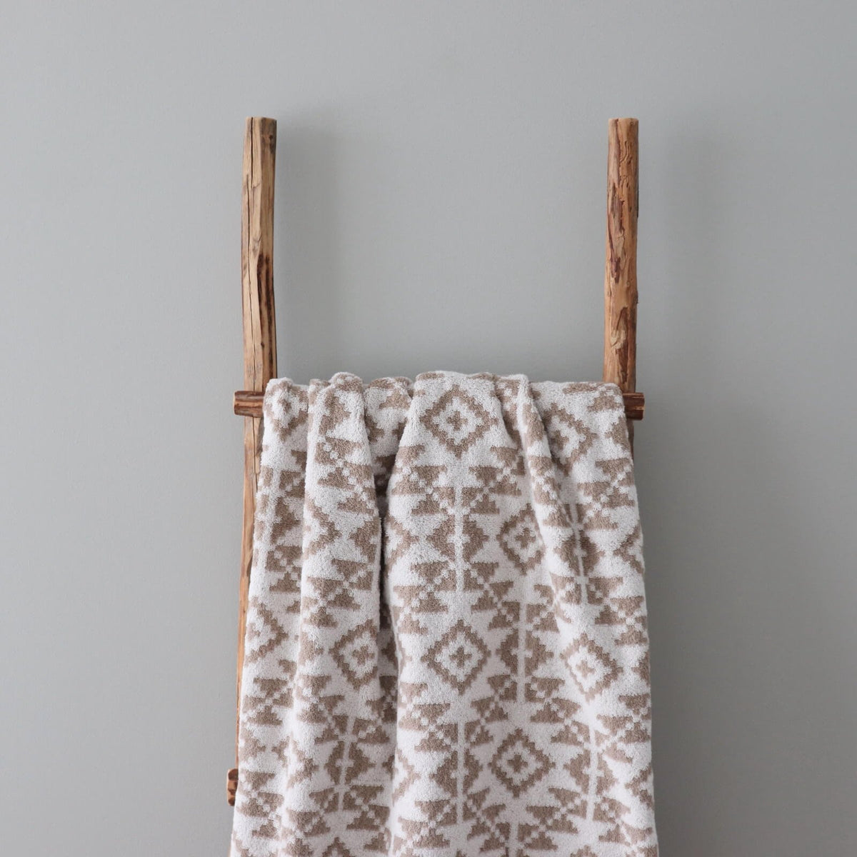 2. Beige and white terry sauna towel with Harju County mitten pattern hanging on wooden ladder against grey wall