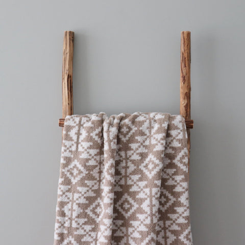 1. Beige and white terry sauna towel with Harju County mitten pattern draped over wooden ladder against grey wall