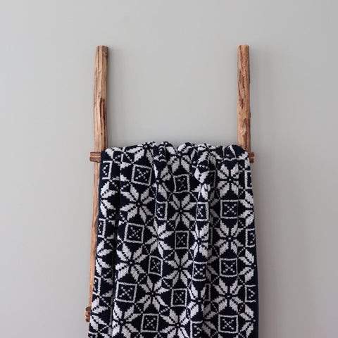 4. Navy sauna towel with Hiiumaa mitten pattern draped over wooden ladder against grey wall