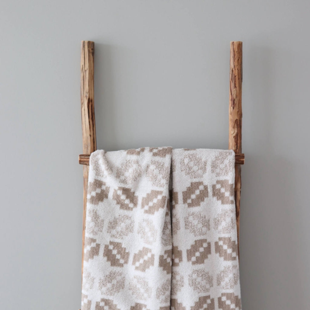 2. White and beige terry sauna towel with Lääne County mitten pattern hanging on a wooden ladder against a grey background