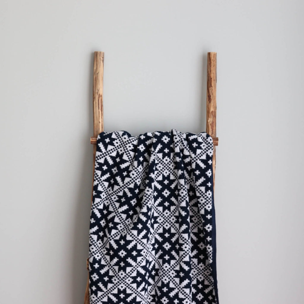 1. Navy and white sauna towel with Pärnumaa mitten pattern draped over wooden ladder against light grey wall