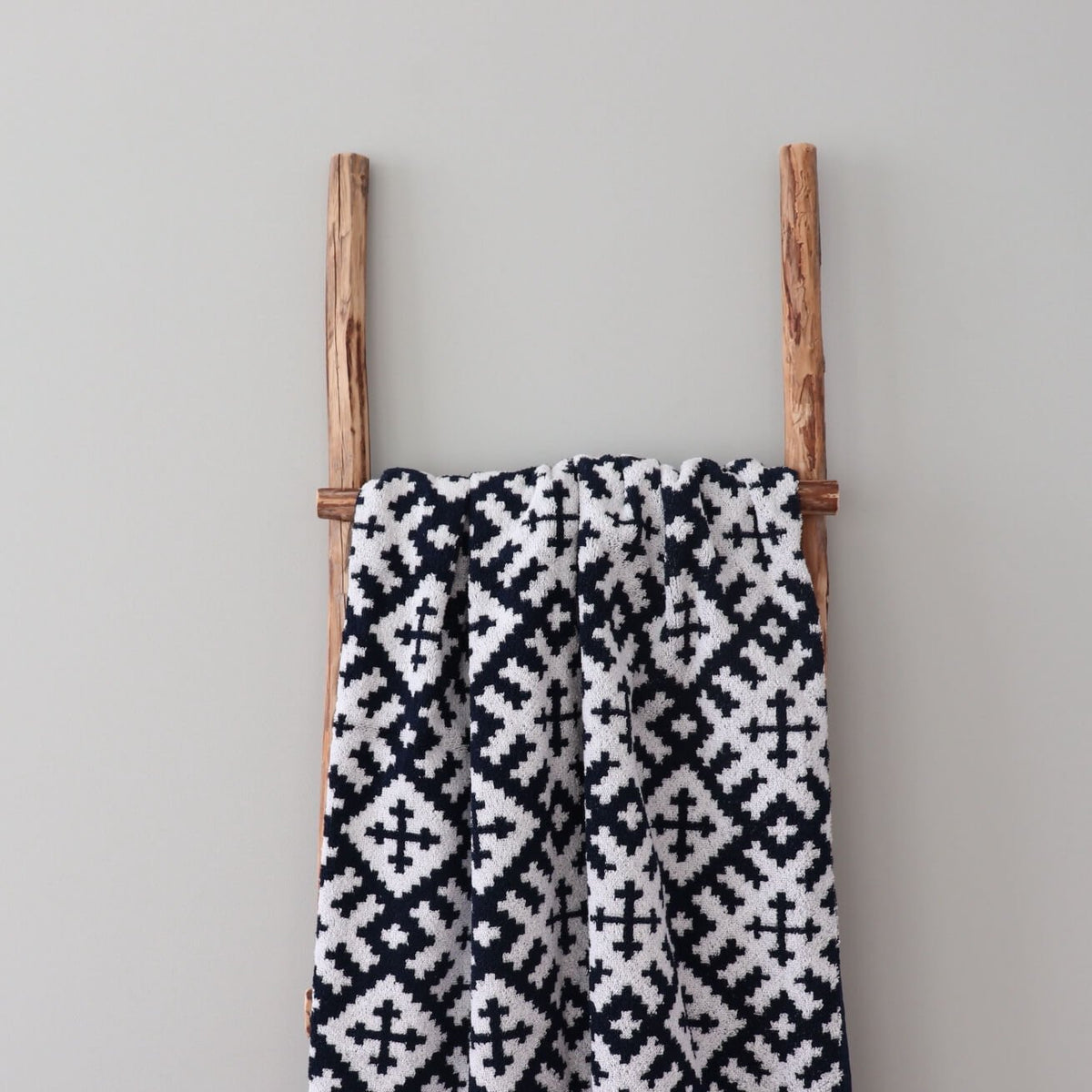 1. Black and white sauna towel with Setumaa mitten pattern draped over wooden ladder against neutral wall