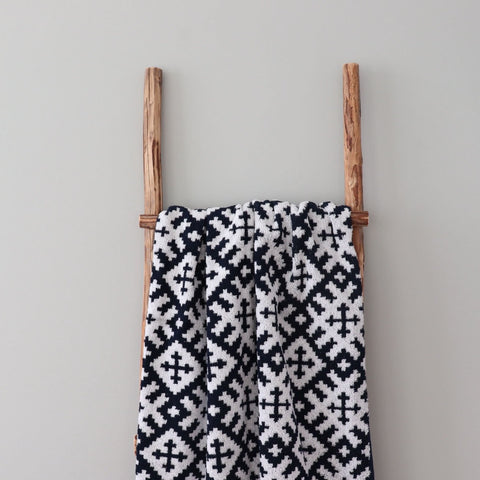 1. Black and white sauna towel with Setumaa mitten pattern draped over wooden ladder against neutral wall