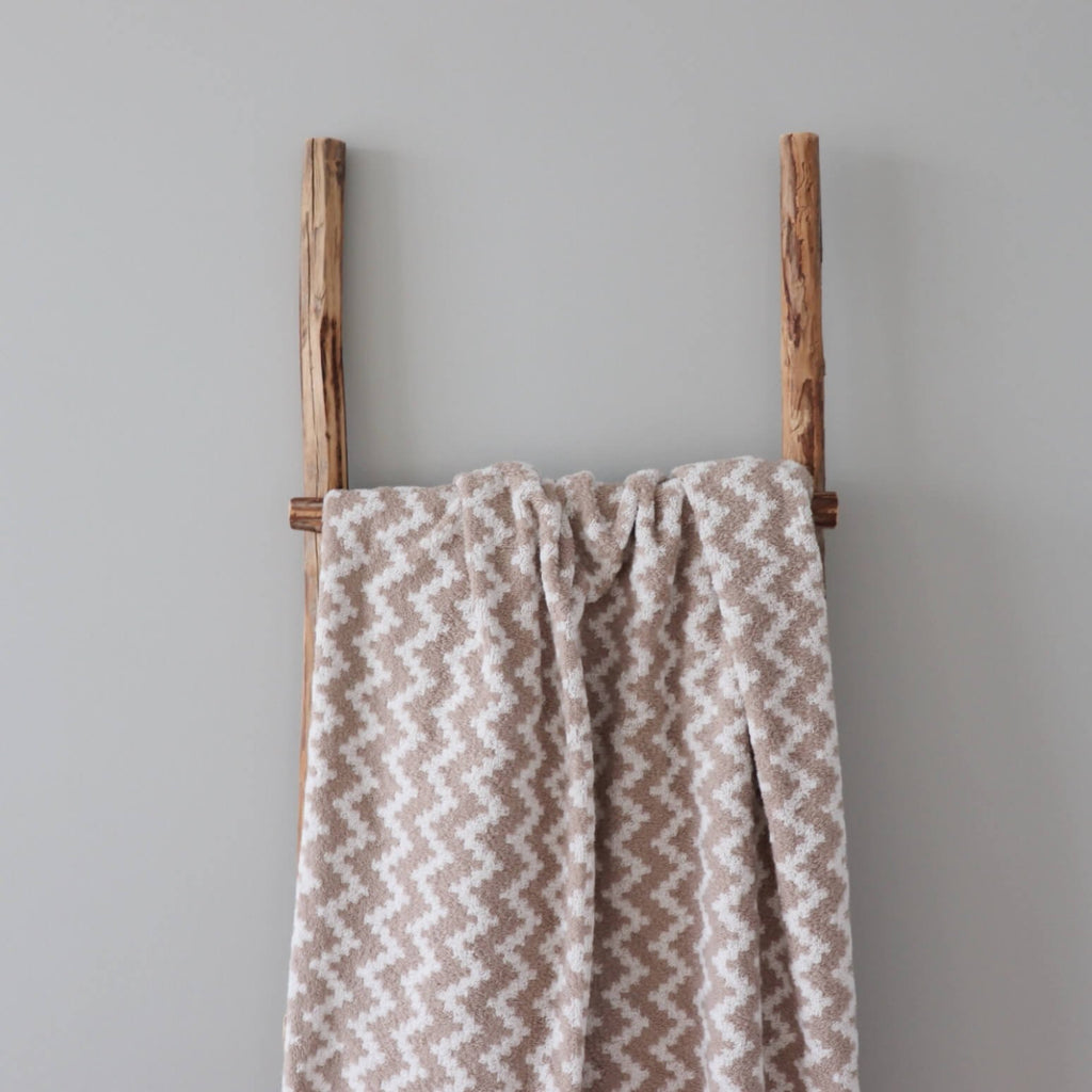 2. Large beige and white sauna towel featuring Tartu County mitten pattern hanging on a wooden ladder in a minimalist setting