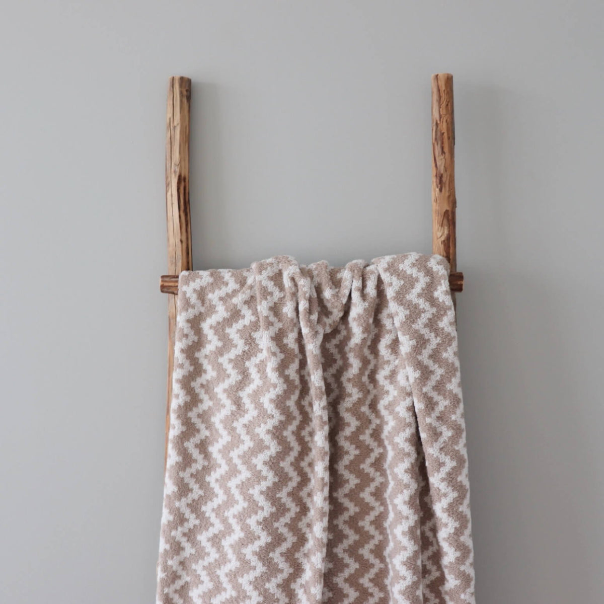2. Large beige and white sauna towel featuring Tartu County mitten pattern hanging on a wooden ladder in a minimalist setting