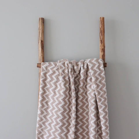 2. Large beige and white sauna towel featuring Tartu County mitten pattern hanging on a wooden ladder in a minimalist setting