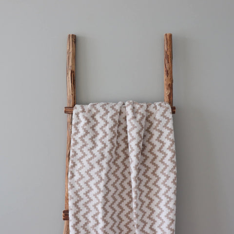 1. Beige and white terry sauna towel with Tartu County mitten pattern draped over a rustic wooden ladder against a neutral wall