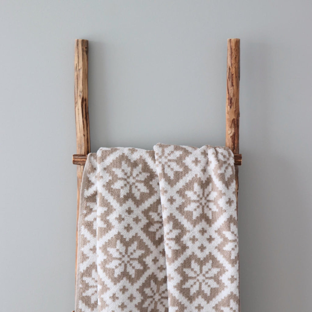 1. Beige and white terry sauna towel with Viljandi County mitten pattern draped over wooden ladder against light grey wall