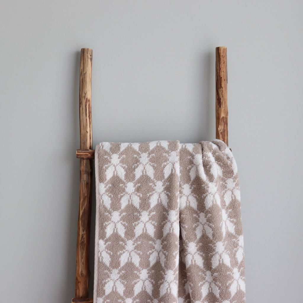 1. Beige and white terry sauna towel with Hiiumaa County mitten pattern draped over a rustic wooden ladder against a grey wall