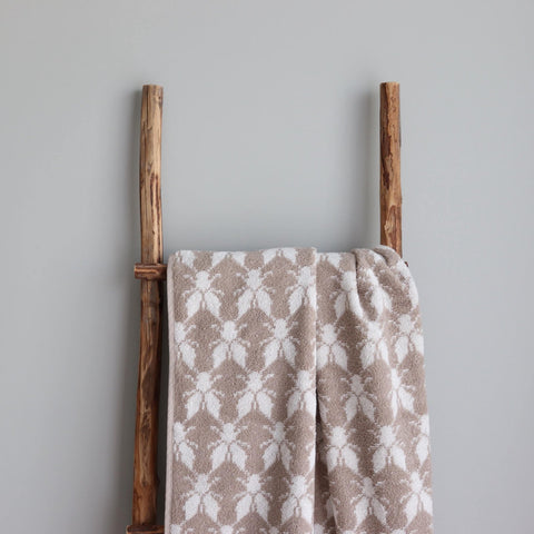 1. Beige and white terry sauna towel with Hiiumaa County mitten pattern draped over a rustic wooden ladder against a grey wall