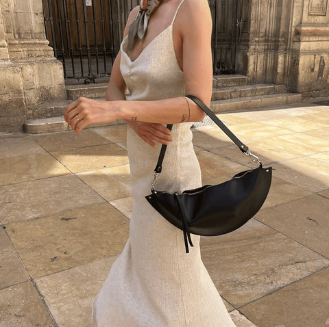 2. Woman holding PYKOK Olivia black leather handbag with short handle, styled with a beige dress outdoors
