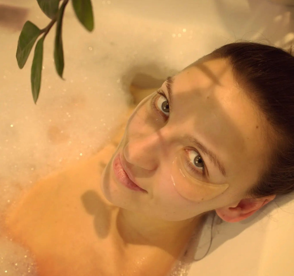 1. Woman relaxing in a bath wearing Turbliss Bog Water Eye Gel Pads, showcasing under-eye treatment
