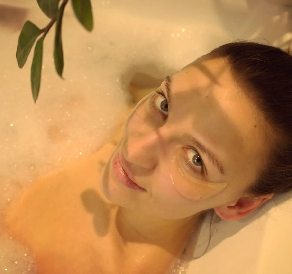1. Woman relaxing in a bath wearing Turbliss Bog Water Eye Gel Pads, showcasing under-eye treatment