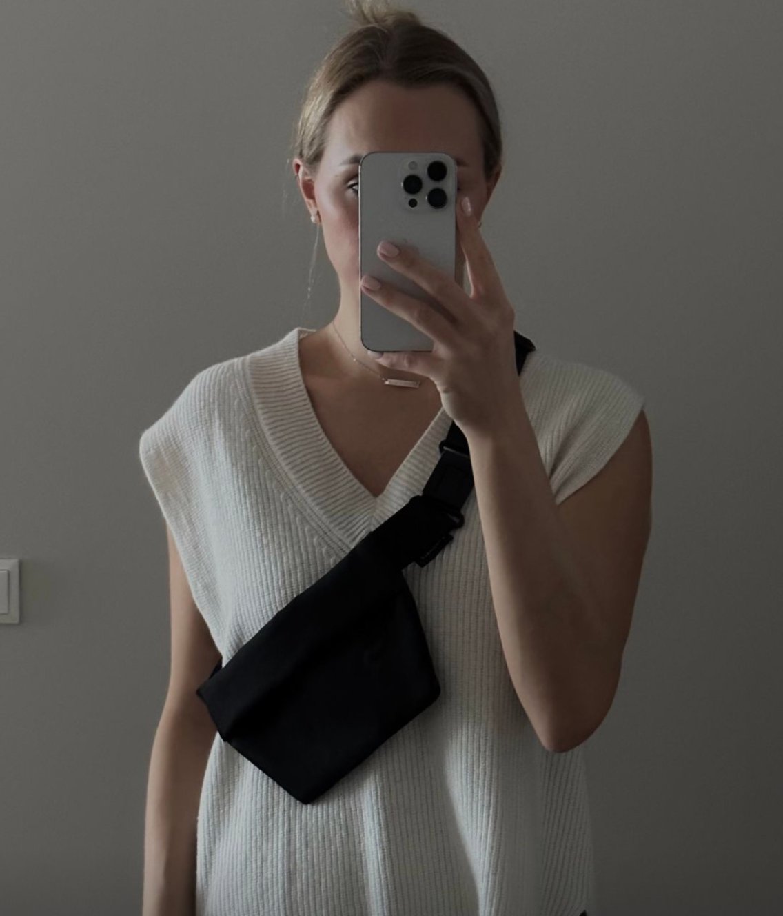 1. Woman wearing Nordhale OSLO MINI Cross Body Bag in black, styled over a white sweater, showcasing versatile wear