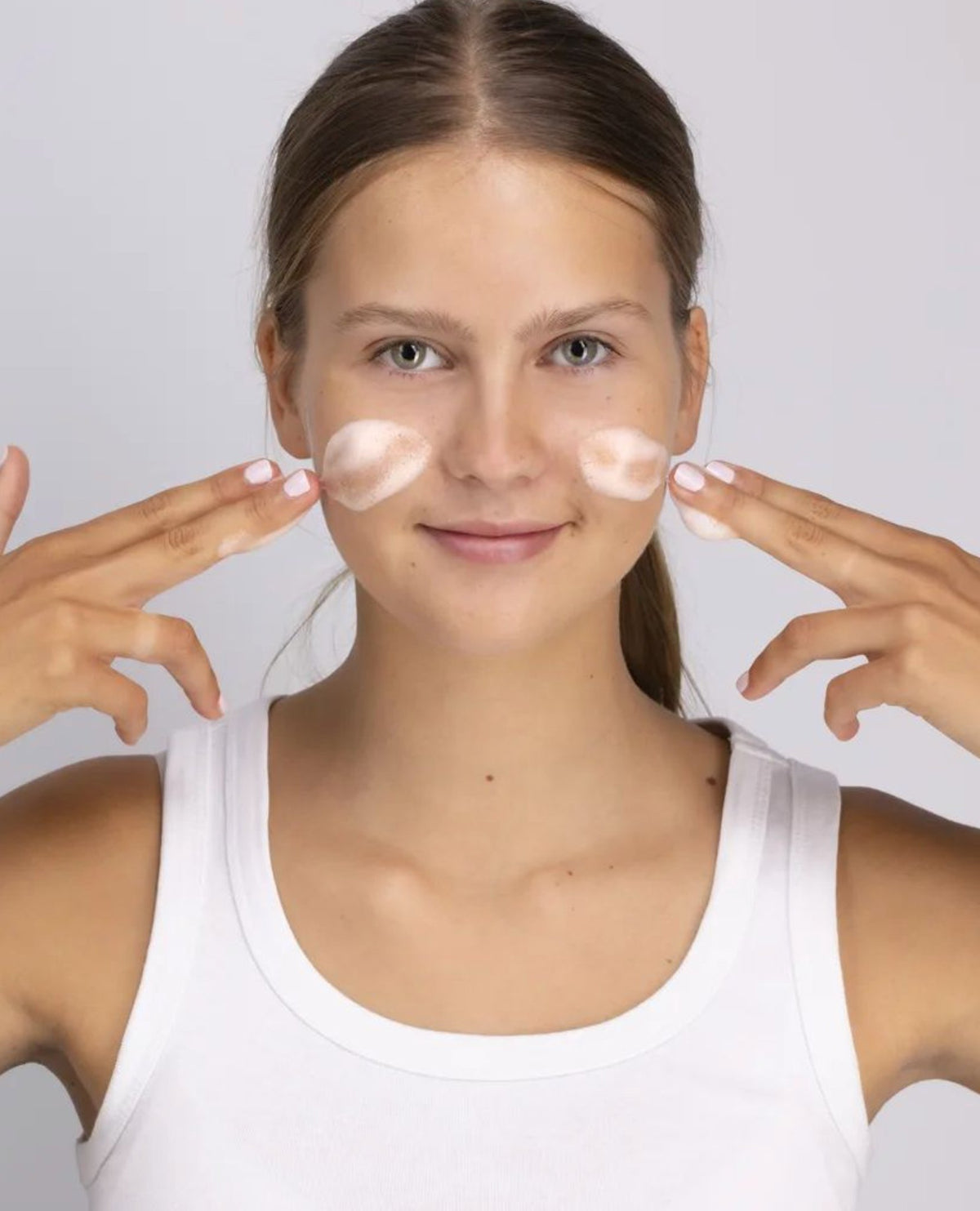 1. Woman applying Berrichi Facial Cleansing Foam to cheeks, demonstrating skincare routine