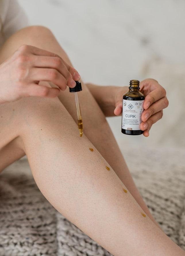 1. Woman applying CUPIK Oregano and Yarrow SOS Oil by MaiWistik to her leg, showcasing skincare routine