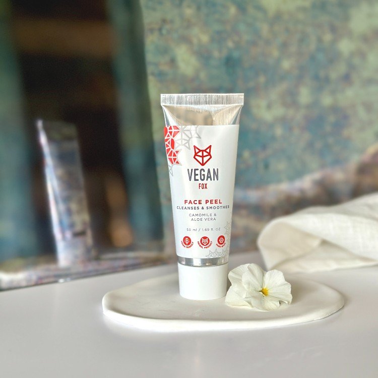 5. Vegan Fox Face Peel tube on a white surface with a single white flower, showcasing its clean beauty appeal
