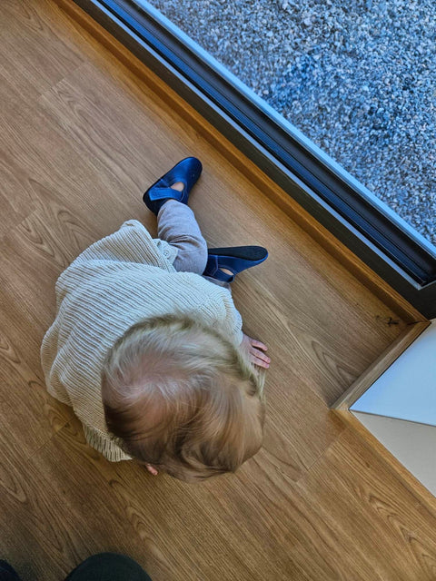 1. Child wearing Omaking Mutsu blue slippers, sitting on wooden floor near window