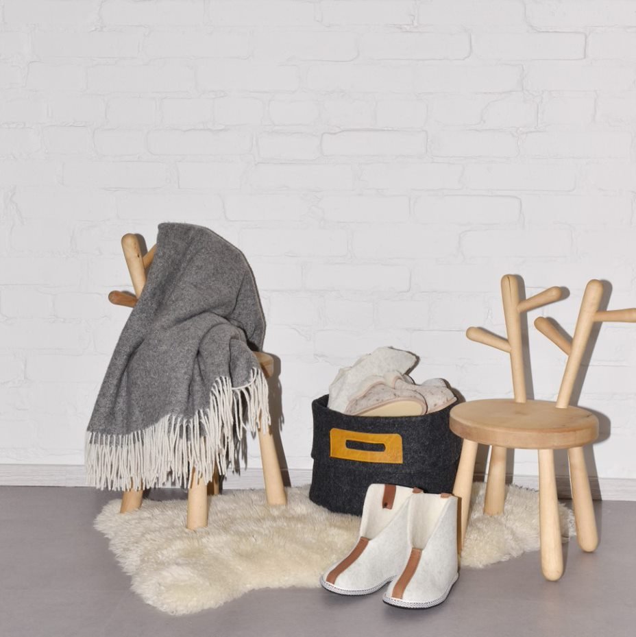 1. Lifestyle image of Wool Felt Omaking Basket in dark grey with cognac leather handle, styled in a cozy room setting with wooden chairs and a blanket