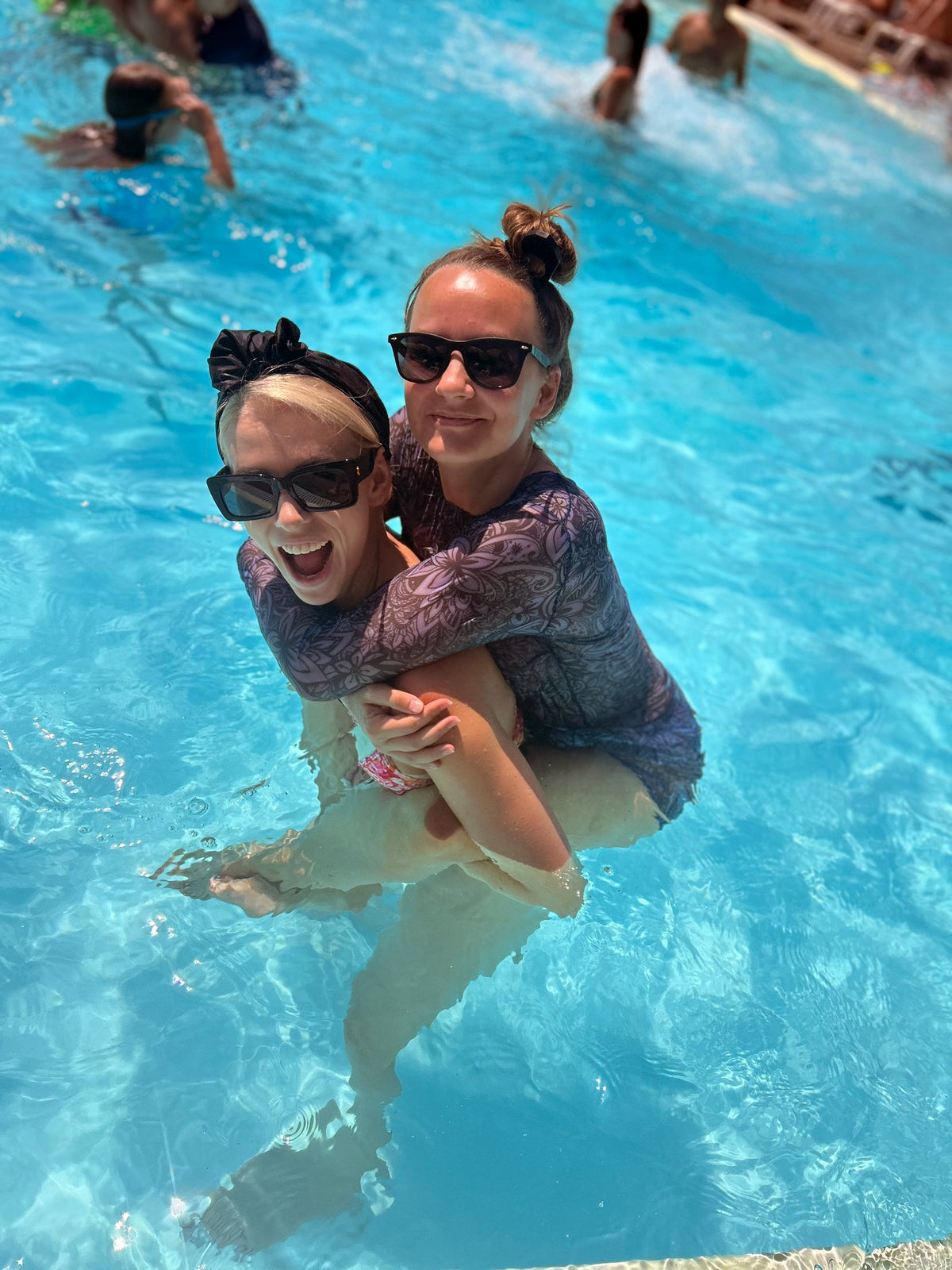 1. Women's tan-through mini leggings in Moonlight Tropica by Smarttan, worn by two women enjoying a pool day