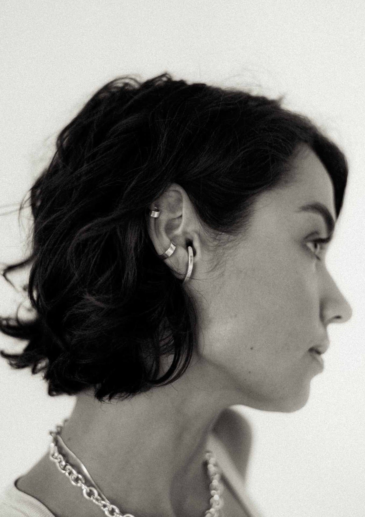 5. Woman with short hair wearing NO MORE flat ear cuff in silver, paired with other silver jewelry, showcasing a contemporary look