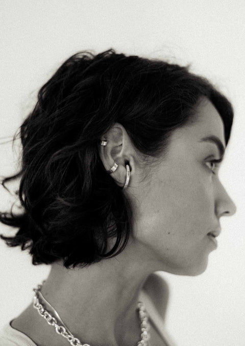 5. Woman with short hair wearing NO MORE flat ear cuff in silver, paired with other silver jewelry, showcasing a contemporary look