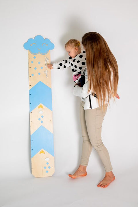 1. Woman holding toddler pointing at light blue growth chart with cloud and raindrop design in studio setting