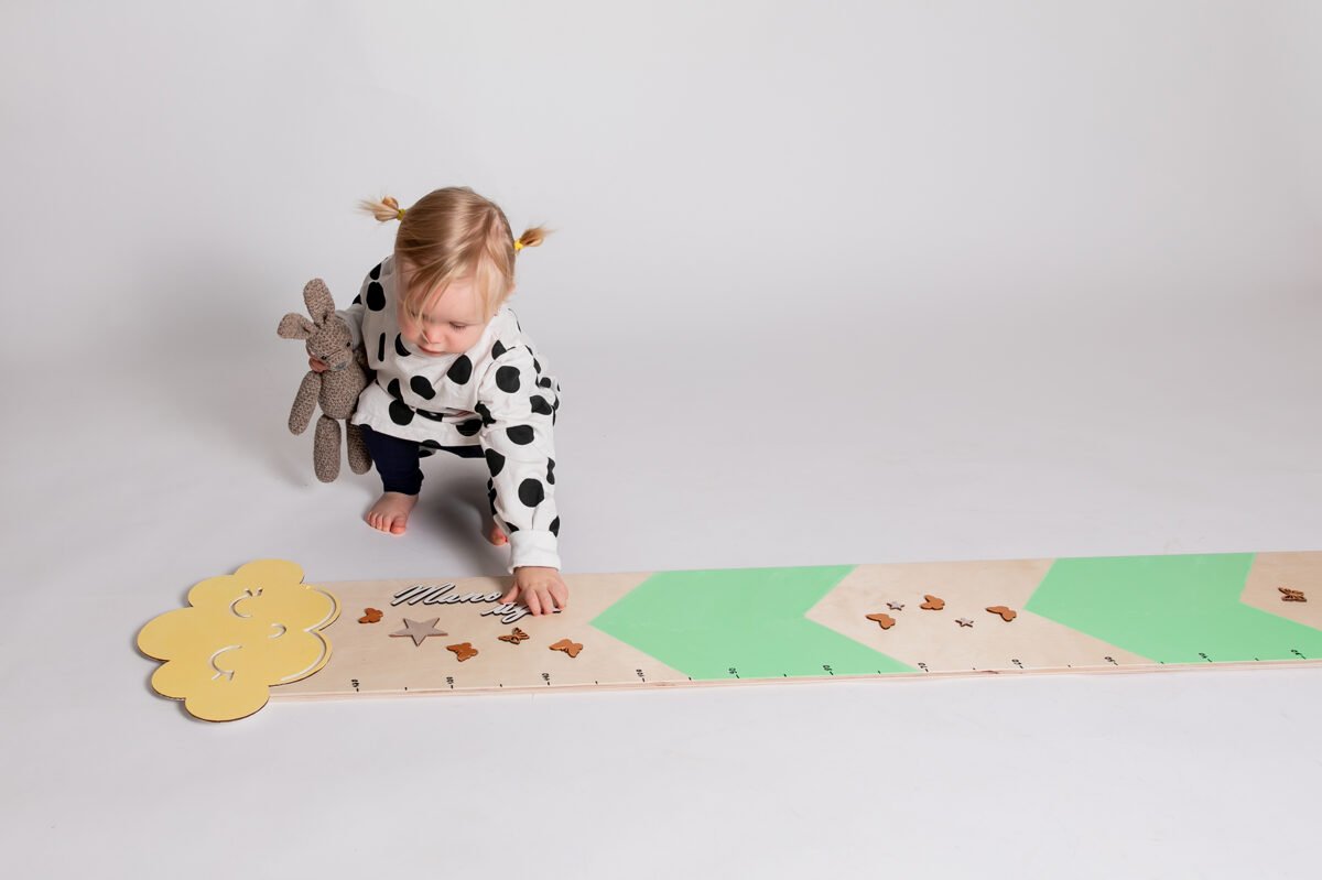 1. Toddler with pigtails wearing polka dot outfit playing with mint green growth chart featuring cloud and raindrop design on studio floor