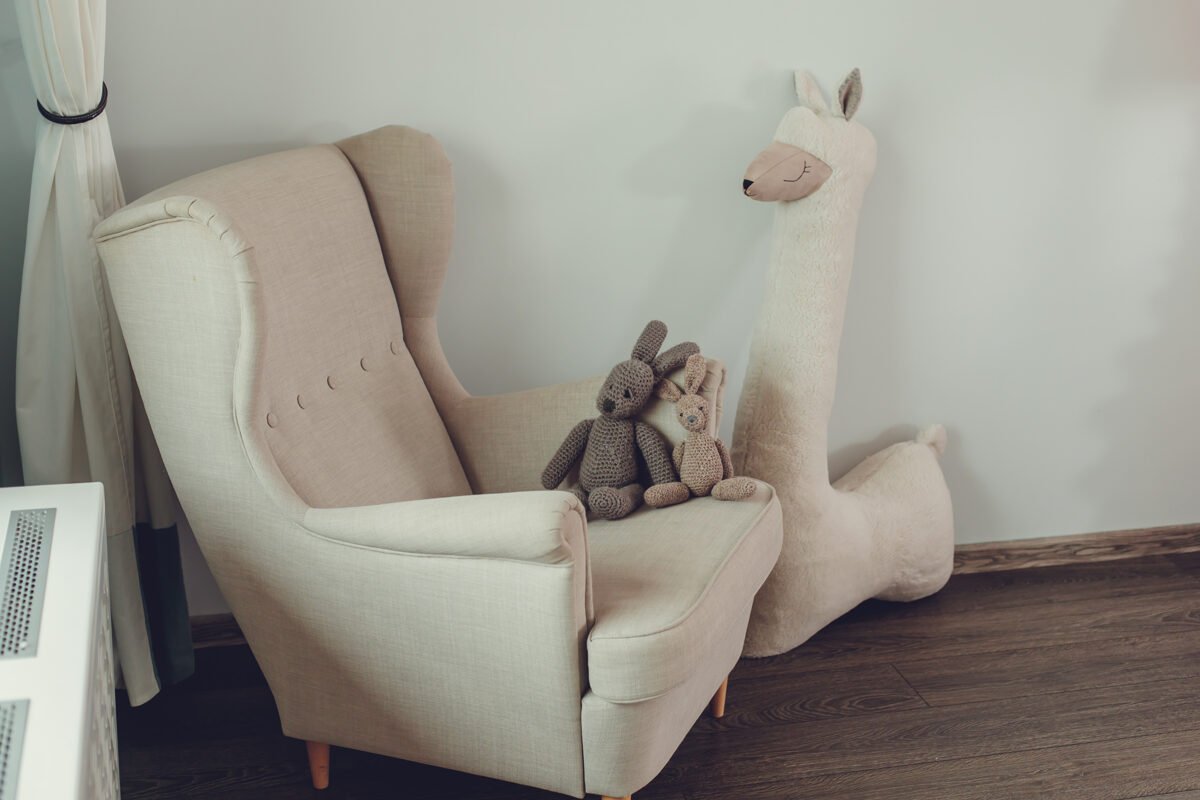3. Beige giant plush alpaca toy next to beige armchair with knitted rabbits