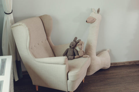 3. Beige giant plush alpaca toy next to beige armchair with knitted rabbits