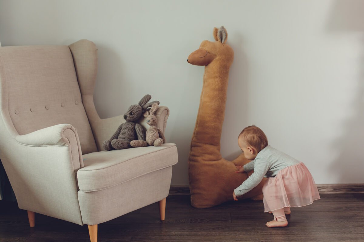 2. Child interacting with rust alpaca plush toy next to armchair in living room