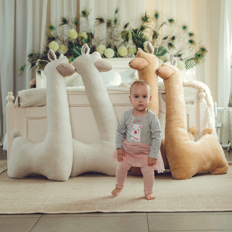1. Woman and child sitting on bed with beige and rust giant plush alpaca toys in cozy room