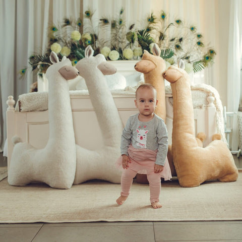 1. Woman and child sitting on bed with beige and rust giant plush alpaca toys in cozy room