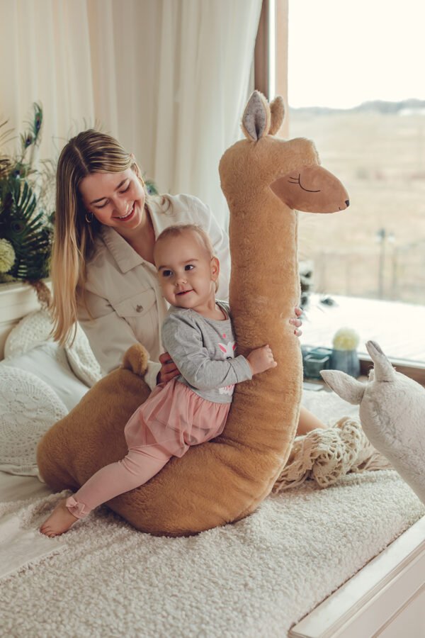 1. Woman and child playing with giant rust alpaca plush toy on bed in cozy room
