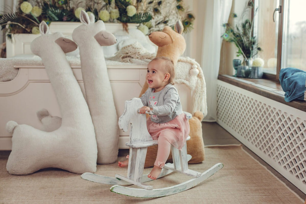 6. Child on rocking horse with beige and rust giant plush alpaca toys in background