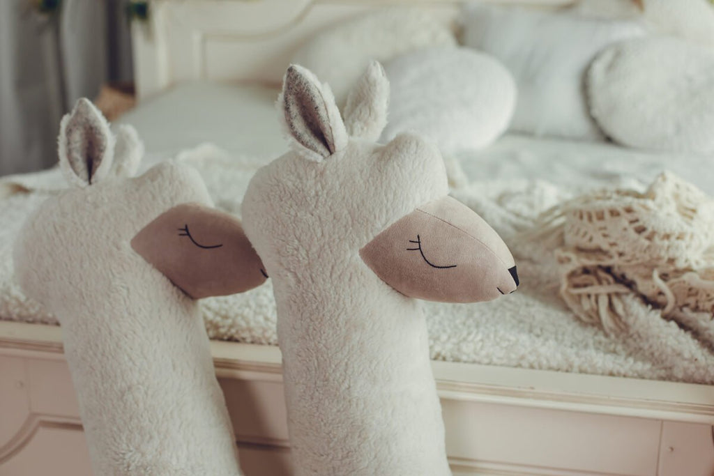 4. Close-up of two beige giant plush alpaca toys with embroidered eyes on bed