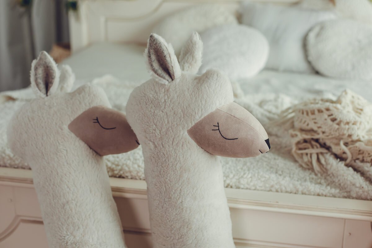 4. Close-up of two beige giant plush alpaca toys with embroidered eyes on bed