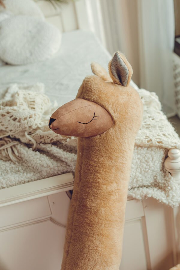 3. Close-up of rust alpaca plush toy head resting on bed edge showing soft texture